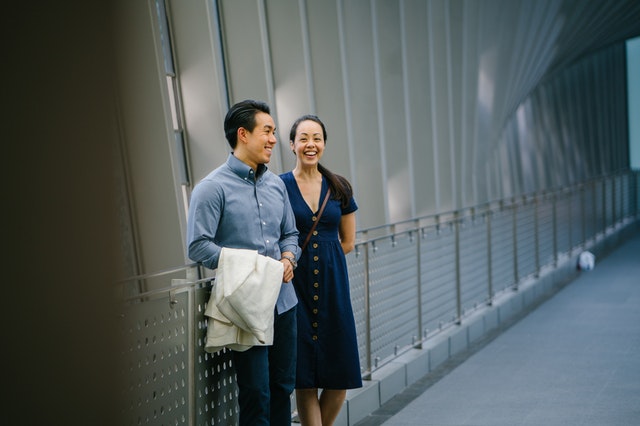 Middle aged oriental couple standing by fence, smiling.